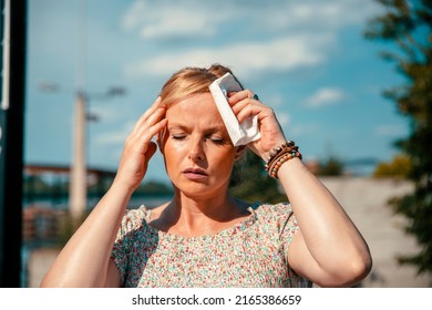 Woman feeling bad pain, heat, woman with heatstroke. Having sunstroke at summer hot weather. Mature Female under sunshine suffering from Headache. Person holds paper tissue on head - Shutterstock ID 2165386659