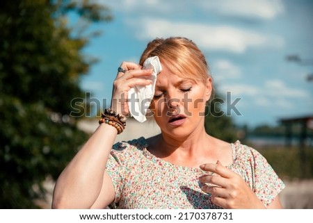 Woman feeling bad pain, heat, woman with heatstroke. Having sunstroke at summer hot weather. Mature Female under sunshine suffering from Headache. Person holds paper tissue on head