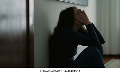 Woman feeling emotional pain sitting on floor home being desperate covering face with shame - Shutterstock ID 2188156045