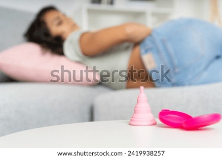 Woman feeling pain for menstruation next to menstrual cup on table