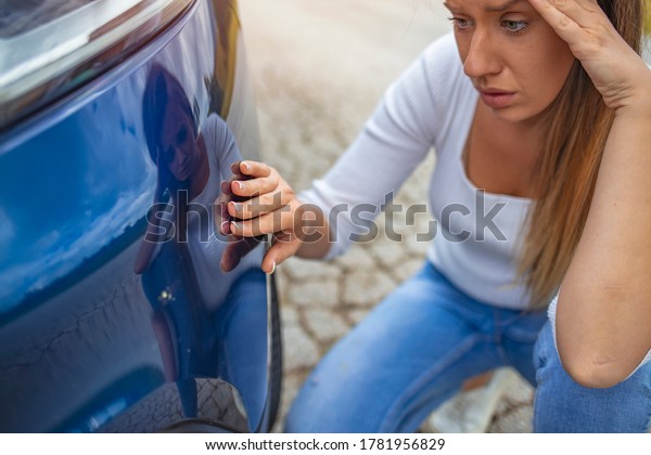 Woman\
feeling sad after scratching her auto. Frustrated young woman\
checking pointing at car scratches and dents outdoors during the\
day, car crash accident, accident\
insurance.