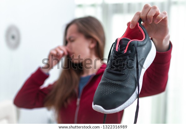 Woman is feeling\
unpleasant smell from sweaty running shoes after long sport\
training and active lifestyle. Footwear needs in cleaning and odor\
removal. Shoe care and\
shine
