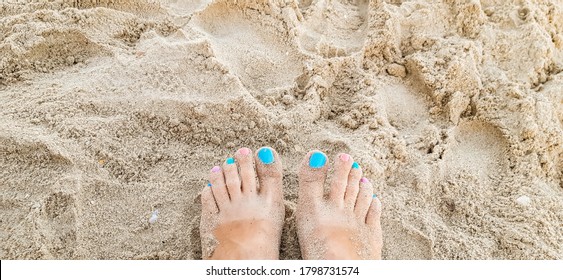 Woman Feet With Blue, Pink Toenails On Natural Beach Sand