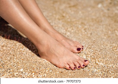 Woman Feet With Dark Pedicure Relaxing On The Sand