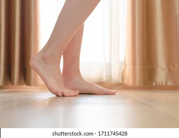 Woman Feet Legs On Wood Floor With Curtain. Barefoot Girl Standing Indoors Inside Modern Home Or Apartment With Wooden Floor.