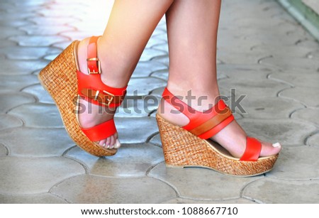 Woman feet in orange leather sandals with straps and cork heels. Outdoor shot. Ready for summer.
