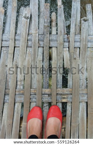 Woman feet in red shoes on weaved bamboo sticks bridge 