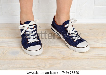 Woman feet shod in classic bllue gumshoes with white shoelaces and standing on toes on a white wood floor. Stand on tiptoe in sports shoes close-up. Front view.