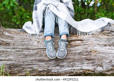 Woman Feet In Sneakers And Jeans On A Log In The Forest