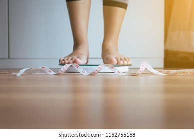 Woman Feet Standing On Weigh Scales With Tape Measure In Foreground,Weight Loss,Body And Healthcare Concept