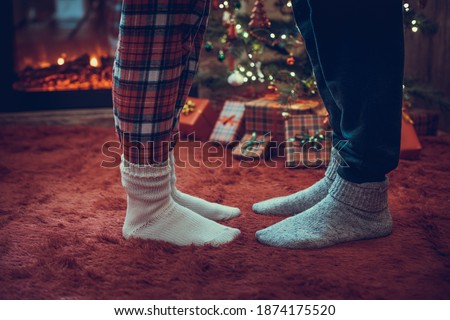 Woman feet standing in tip toe in winter socks on male lags on a fluffy red blanket near a Christmas tree with gifts. Concept 