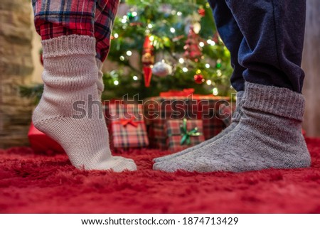 Woman feet standing in tip toe in winter socks near male lags on a fluffy red blanket near a Christmas tree with gifts. Concept 