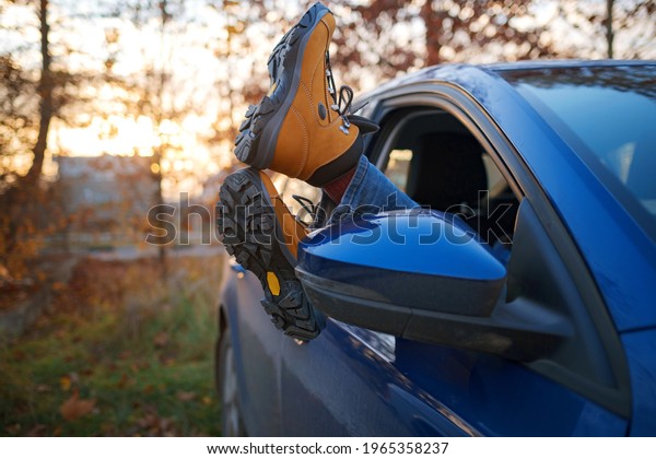 Woman feet in trendy yellow
hiking boots on car door. Feet outside the window at sunset forest.
The concept of freedom of movement. An autumn weekend in
nature.