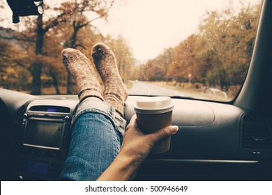 Woman Feet In Warm Socks On Car Dashboard. Drinking Take Away Coffee On Road. Fall Trip. Rain Drops On Windshield. Freedom Travel Concept. Autumn Weekend.