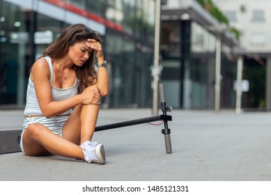 The Woman Fell Off The Electric Scooter. The Injured Woman Sits And Holds Her Knee.