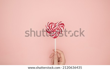 Woman female hand holding heart shaped lollipop on pink background. Creative Valentine's Day romantic composition flat lay top view love holiday celebration, card design