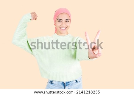 woman fighting cancer gesture of strength with pink handkerchief, optimistic young woman after chemotherapy, beige background
