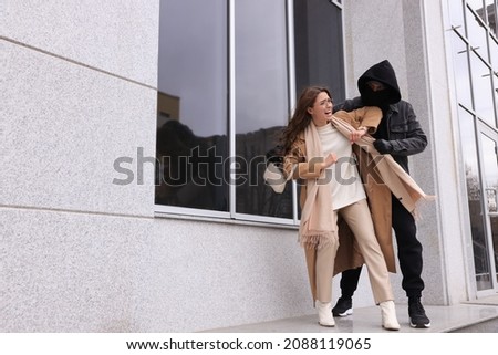 Woman fighting with thief while he trying to steal her bag near building, space for text. Self defense concept