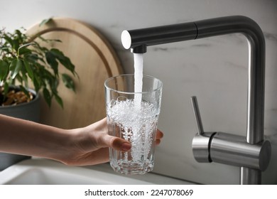 Mujer llenando vidrio con agua del grifo de grifo de grifo en la cocina, en el armario