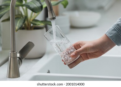 Woman filling glass with water from tap in kitchen, closeup