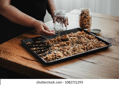 Woman filling a mason jar with homemade granola. Healthy vegan snack easily prepared at home. Visible body parts, hands of an elderly woman.