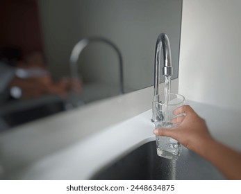 Woman fills glass with tap water from kitchen faucet, blurry background image - Powered by Shutterstock