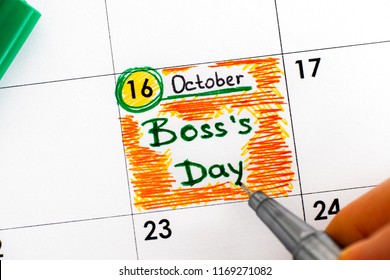 Woman fingers with pen writing reminder Boss`s Day in calendar. Close-up.