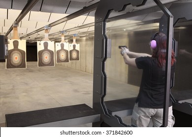 A woman firing a hand gun at an indoor gun range.