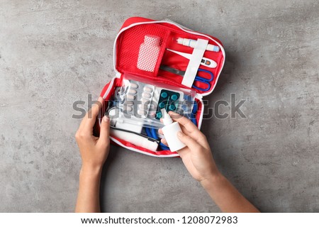 Woman with first aid kit on gray background, top view