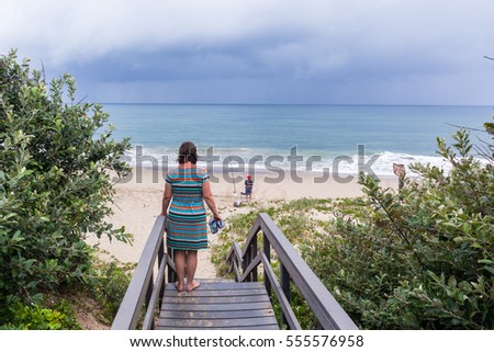 Woman Fisherman Beach Ocean
Woman standing beach staircase steps overlooking fisherman surf fishing remote beach ocean  summer storm landscape