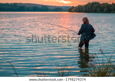 Woman with a fishing rod fishing on the lake on a summer evening