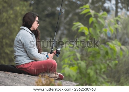 woman fishing sitting on a high rock with the forest in the background