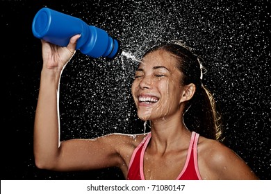 Woman fitness runner drinking and splashing water in her face. Funny image of beautiful female fitness model on black background.