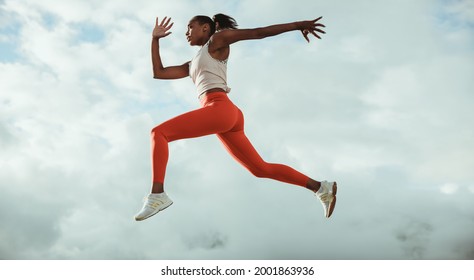 Woman in fitness wear doing running and jumping workout on rooftop against sky. Athletic woman running and jumping outdoors. - Powered by Shutterstock