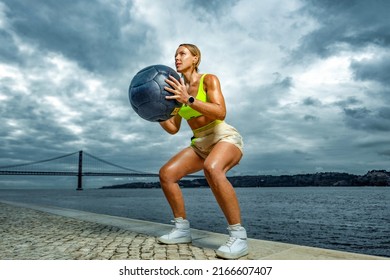 Woman In Fitness Wear Doing Workout With A Heavy Medicine Ball Outdoors.. Sporty Girl With Fit Body In Sportswear Posing On Sky Background.