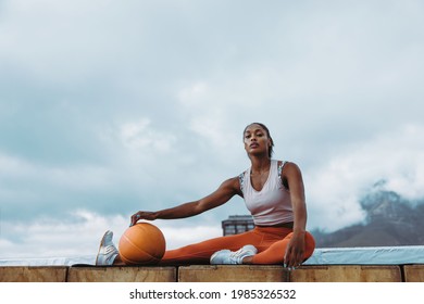 Woman in fitness wear with exercise ball exercising outdoors. Athletic female taking break from workout on rooftop with basket ball. - Powered by Shutterstock