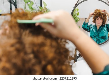 Woman fixes her hair in the bathroom in front of the mirror touches up her curly red hair - Powered by Shutterstock