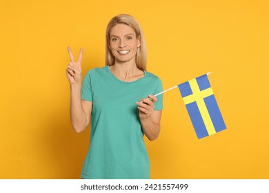 Woman with flag of Sweden showing V-sign on yellow background