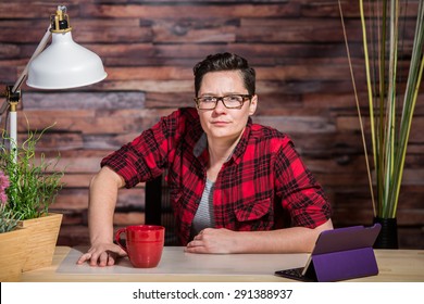 Woman In Flannel Shirt Leaning On Modern Desk With Red Cup