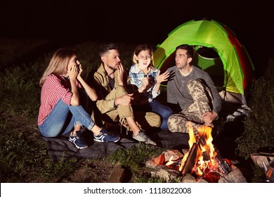 Woman with flashlight telling scary story for her friends near bonfire at night. Camping season