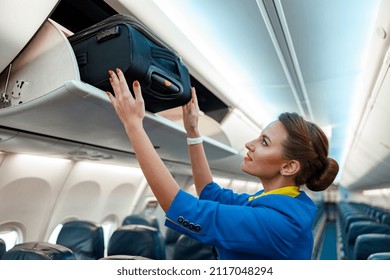 Auxiliar de vuelo o azafata de aire colocando la bolsa de viaje en el casillero de equipaje de carga mientras se encuentra en el salón de pasajeros del avión