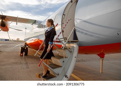 Woman Flight Attendant Standing On Airplane Stairs At Airport