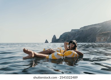 Woman Floating Inflatable Sea - Woman relaxing on a yellow inflatable raft in the ocean, with cliffs in the background. - Powered by Shutterstock