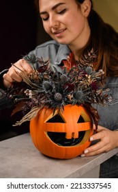 woman florist gently decorate lovely autumn arrangement of thistles flowers and plants in bright orange pumpkin with carved eyes and mouth. Beautiful floral decor for halloween. Close-up - Shutterstock ID 2213337545