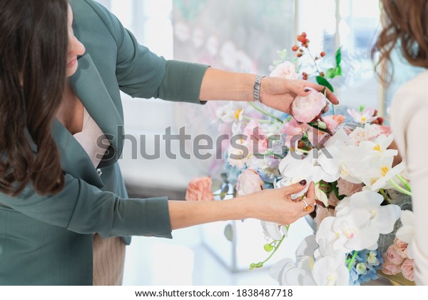 Woman florist on wedding makes flower composition
for bride and groom from roses, tulips, peonies, orchids on table.
Decorators working at event: birthday, anniversary, party. Hand
with floral tattoo.