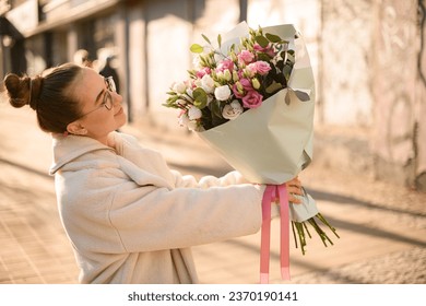 Woman florist rises up bouquet of fresh eustoma flowers in cream and pink colors. Side view. Blurred background - Powered by Shutterstock