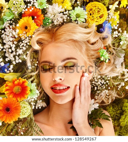 Woman with flower hairstyle lying on grass. Art photo.