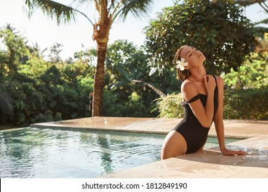 Woman with flower in her hair relaxing in outdoor swimming pool in Bali luxury resort