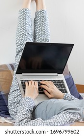 A Woman In Flowered Nightwear Is Lying On Her Back, With Her Legs Raised Straight Up And Work On Her Laptop. Concept Of Staying At Home During Pandemic.