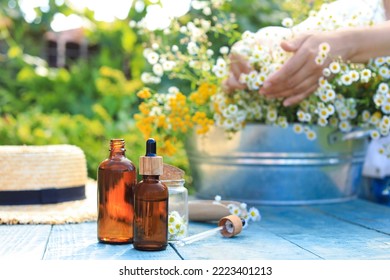 Woman With Flowers Near Table Outdoors, Focus On Bottles Of Chamomile Essential Oil